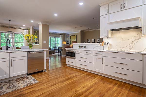 White kitchen cabinets with honey colored floor and stainless steel appliances looking through to a family room and a wall of windows